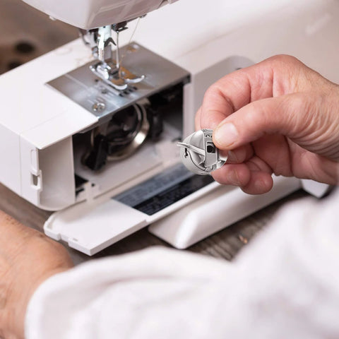 Close-up of a stainless steel sewing machine bobbin case for front-loading machines, held in hand.