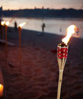 Two Pack Bamboo Tiki Torch Oil Lamp Set For Garden And Patio Outdoor Lighting with Citronella Scented Fuel on beach at sunset
