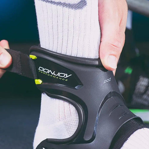 Close-up of Performance POD Ankle Brace being fastened on a socked foot with molded TPU shell for stability in sports.