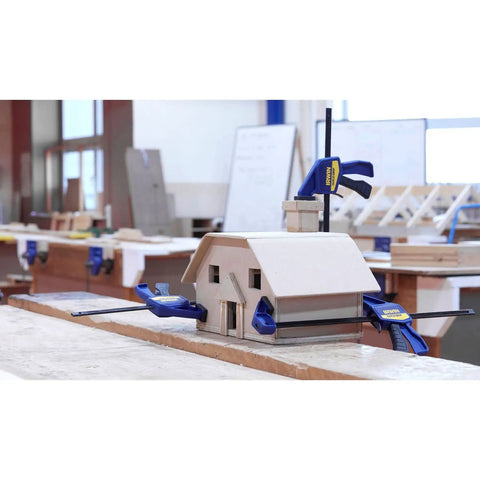 Six Inch Mini Bar Clamp Two Pack With One Hand Quick Release Trigger securing a wooden house model in a workshop.