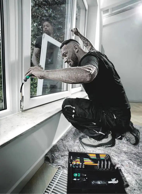 Man using Extra Slim Bit Holding Screwdriver With Flexible Shaft And Magnetic Bit Holder to fix window, with tool kit nearby.