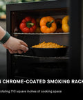 Hand placing dish in Digital Electric Vertical BBQ Smoker With Patented Side Wood Chip Loader And Chrome Racks 710 Square Inches
