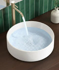 Round Vessel Sink For Bathroom 15.75 Inch Ceramic Bowl With White Gloss Finish filled with water, gold faucet running, above countertop.