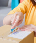Blue retractable box cutter knife with metal blade opening a cardboard box.