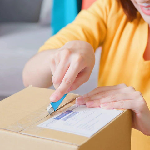 Blue retractable box cutter knife with metal blade opening a cardboard box.