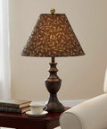A decorative table lamp with a patterned brown shade on a side table next to a couch in a cozy living room setting.