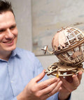 Globus Mechanical Globe Model Kit 3D Puzzle With Laser Cut Wood Pieces No Glue Or Tools Needed Self Contained Gearing Rotating World Globe Build For Adults And Hobbyists Educational Hands On World Globe Puzzle Set, man holding assembled wooden globe