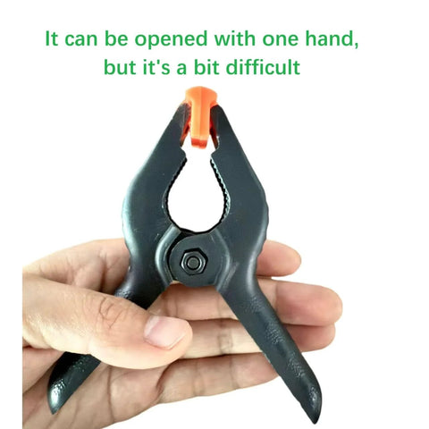 Front view of a 4.5-inch black plastic spring clamp with orange jaw, held by hand.