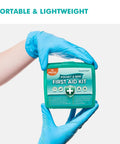 Front view of a compact green plastic first aid kit labeled Pocket & Mini First Aid Kit (70 pieces) held by blue-gloved hands.