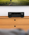 Front view of 7.2 Channel AV Receiver With Built-In HEOS And 8K HDMI Dope Wireless Streaming Dolby Atmos HDR10 Plus Dynamic HDR DTS X WiFi And Bluetooth Plug And Play Setup For Small To Medium Rooms And Smart Home Vibes on wooden cabinet