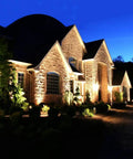 JUDYSSY Outdoor Solar Flood Lights illuminate a stone house landscape, highlighting gardens and pathways at night.
