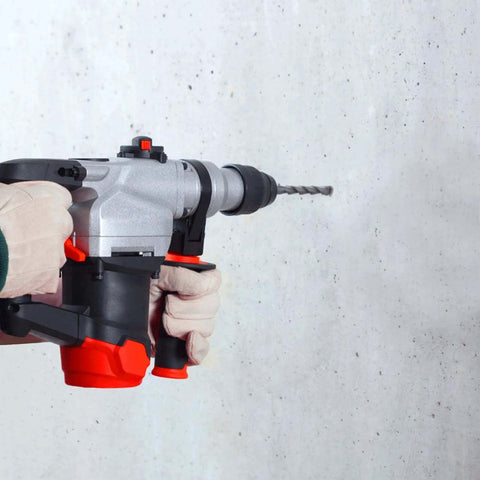 Side view of an SDS Plus hammer drill with a masonry bit held by gloved hands against a concrete wall.