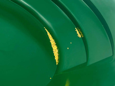 Close-up of green pan from Dual-Sided Gold Panning Kit With Vanishing Riffles For Maximum Gold Recovery, showing trapped gold flakes.