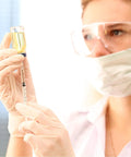 Close-up of a 1 ml syringe with a 30G 5/16 inch needle, drawing yellow liquid from a vial with gloved hands.