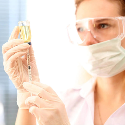 Close-up of a 1 ml syringe with a 30G 5/16 inch needle, drawing yellow liquid from a vial with gloved hands.