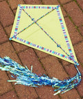 Yellow kite with striped edges and blue tail laying on brick pavement.