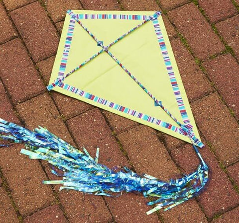 Yellow kite with striped edges and blue tail laying on brick pavement.