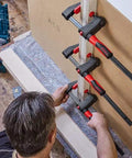 Man using GK60 24 Inch GearKlamp 4 Pack Clamps for Tight Spaces with Separate Handle and Quick Release Shift Button on wood panel.