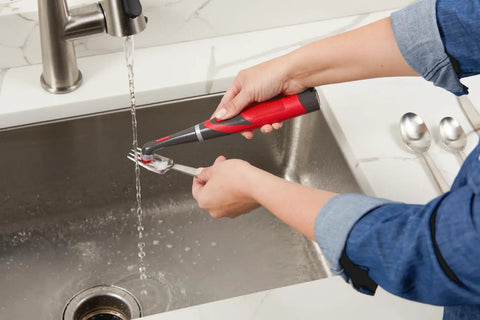 Person using attachable grout head for cordless power scrubber on a fork over a kitchen sink