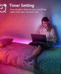 Woman using a laptop in a bedroom with 65 Foot Color Changing LED Light Strip With Remote And App Control For Bedroom Party Setup Dope RGB Lighting With 24V Power Supply Indoor Mood Lighting For Home Decor And Music Sync installed on the wall.