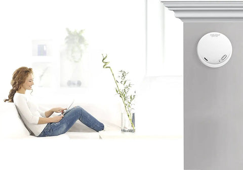10 Year Carbon Monoxide And Photoelectric Smoke Alarm With Sealed Battery No Battery Replacements For 10 Years Frustration Free And Nuisance Free Detection UL Listed Home Safety Detector For Peaceful Kitchens And Living Spaces installed on ceiling in living room next to person sitting on couch