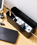 Medium black cable management box with surge protector inside on wooden desk, part of Two Pack Cable Management Box Organizer Set.