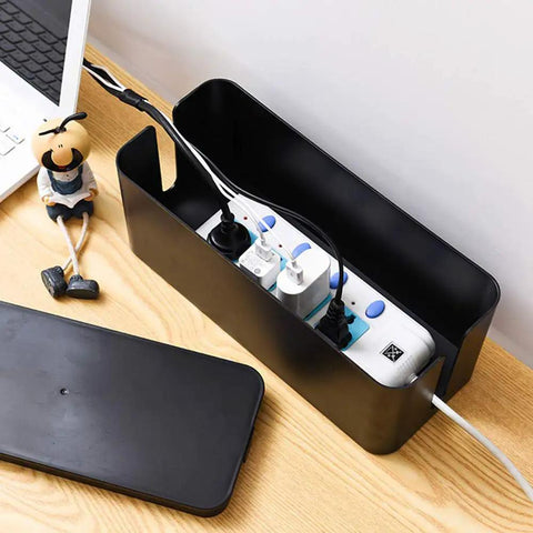 Medium black cable management box with surge protector inside on wooden desk, part of Two Pack Cable Management Box Organizer Set.