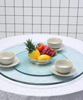 Bombproof Tempered Glass Lazy Susan Turntable with Thickened Serving Plate on table, featuring fruit and bowls, smooth rotating carousel