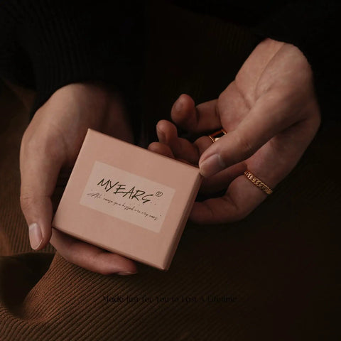 Hands holding a pink jewelry box, labeled 'MYEARS', potentially containing Gold Huggie Hoop Earrings For Women With Chunky Link Chain Cubic Zirconia 14K Gold Plated Hypoallergenic Everyday Jewelry That Goes From Casual To Dressy And Stacks With Any Look.