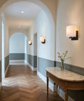 AuroraSpher Indoor Hardwired Modern Milky White Acrylic Black Wall Sconce elegantly lit hallway with wooden floor and archway.