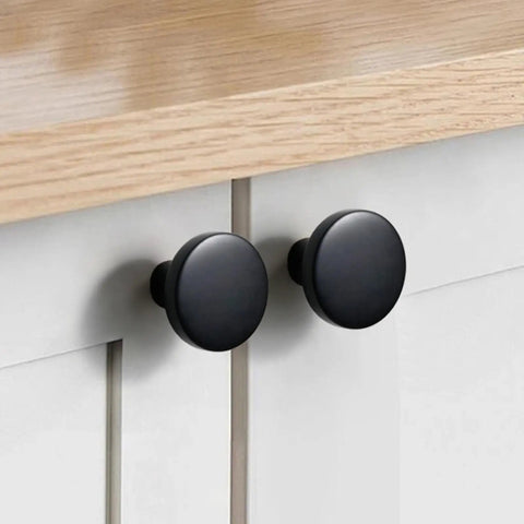 Close-up of matte black cabinet knobs set ten pack one and a quarter inch round solid zinc alloy drawer pulls on a wooden cabinet