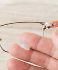 Close-up of a hand holding a nose pad from a 527 Piece Eyeglass Repair Kit With Glasses Screws, Tiny Screwdriver Set, Tweezers, Cleaning Cloth, And Portable Case For Quick On The Go Lens And Frame Fixes next to eyeglass frame.