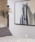 Bedroom with abstract horse painting on wall, grey geometric bedding, white lamp and brick wall detail.
