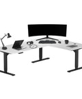 Badass Electric Sit To Stand L Shaped Corner Desk With Smooth Height Adjustment, Spacious 78 By 60 Inch Work Surface For Epic Home Office Workflow And Multi Monitor Grind Stations In Sleek Black Frame And Warm White Finish, showing a corner office setup with laptop and monitors.