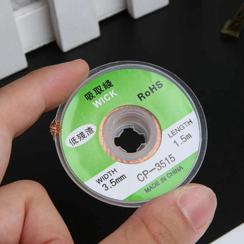 Hand holding a spool of 4Pcs 3.5mm Desoldering Braid Solder Removal Wick Wire Kit 1.5m Long for PCB cleaning and repair.
