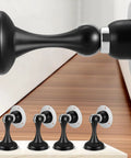 Four Pack Magnetic Door Stop No Drilling With 3D Adhesive Tapes Keeps Doors Open And Silent Easy Install Durable Stainless Steel Mount With Included Screws Black Finish Great For Home And Office, showing a set of four black magnetic door stops installed on a wooden floor with one in close-up view.
