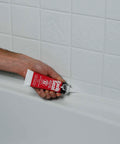 Applying Kwik Seal Kitchen And Bath Adhesive Caulk White 2.8 Oz Waterproof Sealant That Bonds Like Glue And Seals Like Caulk For Sinks, Tubs And Showers No Mess Quick Fix For Moisture Prone Areas on bathtub seam, close-up view.