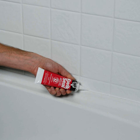 Applying Kwik Seal Kitchen And Bath Adhesive Caulk White 2.8 Oz Waterproof Sealant That Bonds Like Glue And Seals Like Caulk For Sinks, Tubs And Showers No Mess Quick Fix For Moisture Prone Areas on bathtub seam, close-up view.