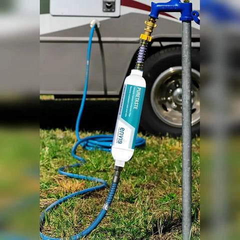Heavy Duty Catalytic Carbon KDF Inline RV Water Filter attached to a water source with a blue hose on grass.