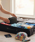 Open black suitcase on a bed with folded clothes; passport and a colorful cap nearby.