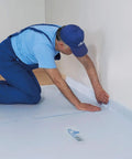 A worker applying Temporary Floor Protection Roll 36 Inch By 100 Foot Anti Slip Surface Easy To Apply Paint Proof Reusable Durable Material Covers Up To 300 Square Feet No Mess Cleanup During Remodeling And Moving around room edges.