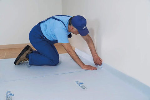 A worker applying Temporary Floor Protection Roll 36 Inch By 100 Foot Anti Slip Surface Easy To Apply Paint Proof Reusable Durable Material Covers Up To 300 Square Feet No Mess Cleanup During Remodeling And Moving around room edges.