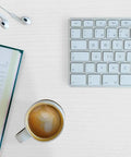 Desk with a keyboard, coffee, and notebook on White Wood Grain Peel And Stick Wallpaper 15.7 In By 118 In Waterproof Vinyl surface