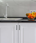 Modern kitchen with sink and fruit bowl, featuring matte black 30 Pack 5 Inch Kitchen Square Cabinet Handles on white cupboard doors.