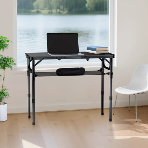 Tri Fold Aluminum Camping Table With Storage Net and Adjustable Heights, set up as a desk near a window with a lake view.