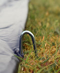 Close-up of metal stake securing a Trampoline Weather Cover 15Ft Round All Season Protection No Fuss Waterproof PVC Shield to grass