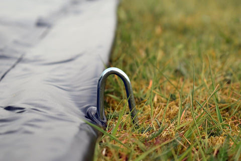 Close-up of metal stake securing a Trampoline Weather Cover 15Ft Round All Season Protection No Fuss Waterproof PVC Shield to grass