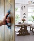 Person holding 9 Inch Sliding Barn Door Handle Set in Black Frosted Finish on wooden door, view of interior room