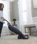 Person using an upright vacuum with Vacuum Belt 2 Pack Genuine OEM Replacement Part 301291G on carpet, bright living room.