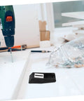 Close-up of a black and silver latch on a white table with a drill. Two Pack Toggle Clamp Latches For Tool Box Storage Rack And Gear Case Noise Reducing Rubber Tips Stainless Steel Construction Secure Draw Latch Clasp For Cabinets Boxes Coolers And Equipment.